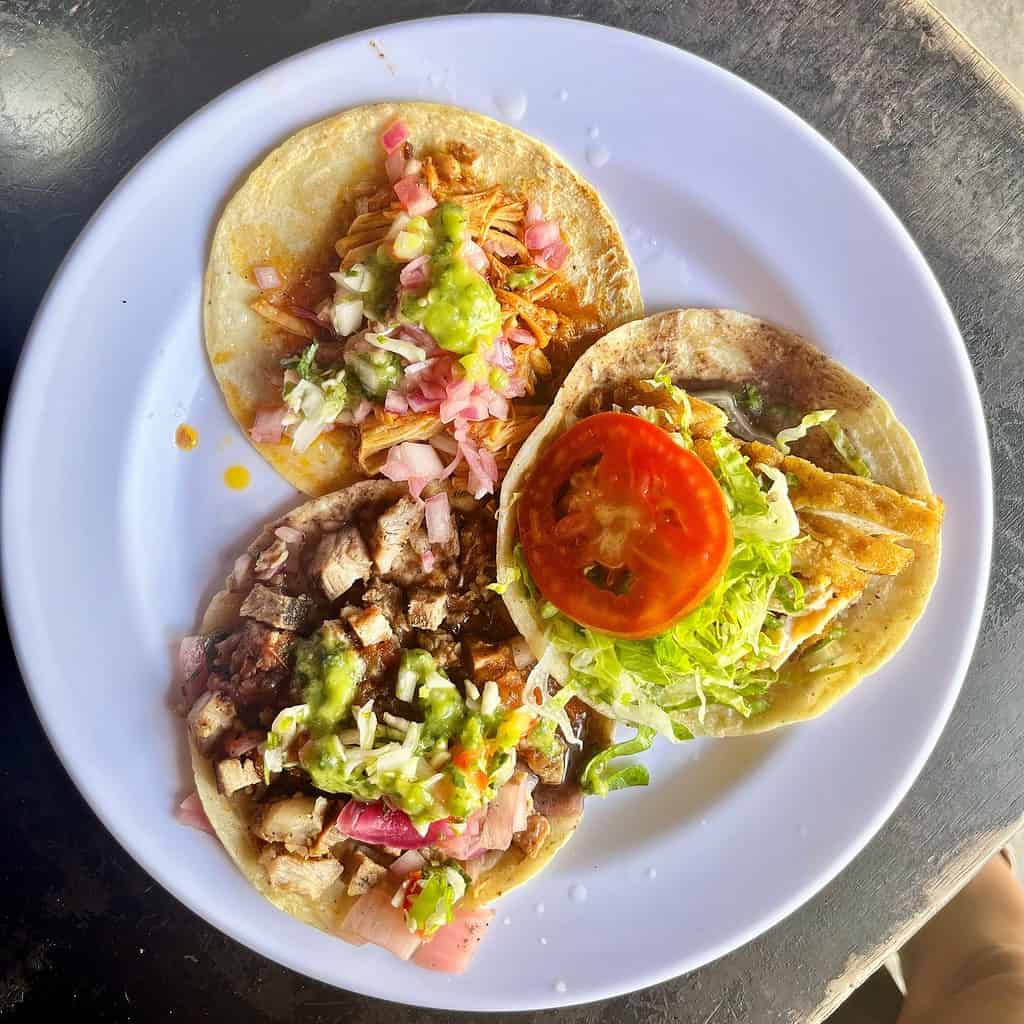 Tacos al pastor with fresh toppings, grilled meat, and vibrant vegetables on corn tortillas, served on a white plate at a Mexican restaurant.
