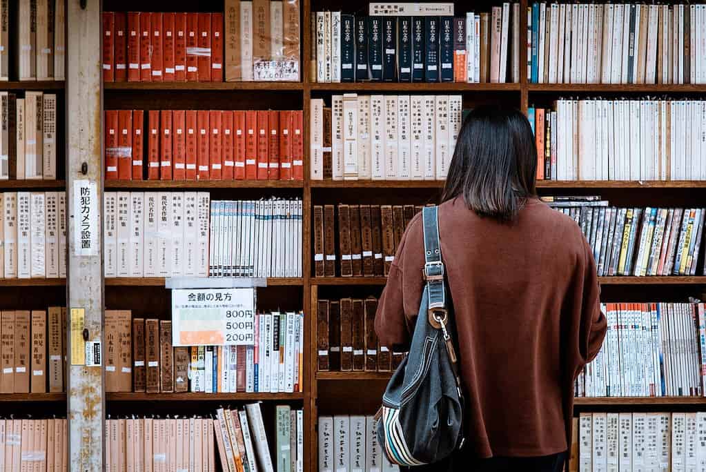 A woman reading books at a library shelf filled with Japanese books and magazines.