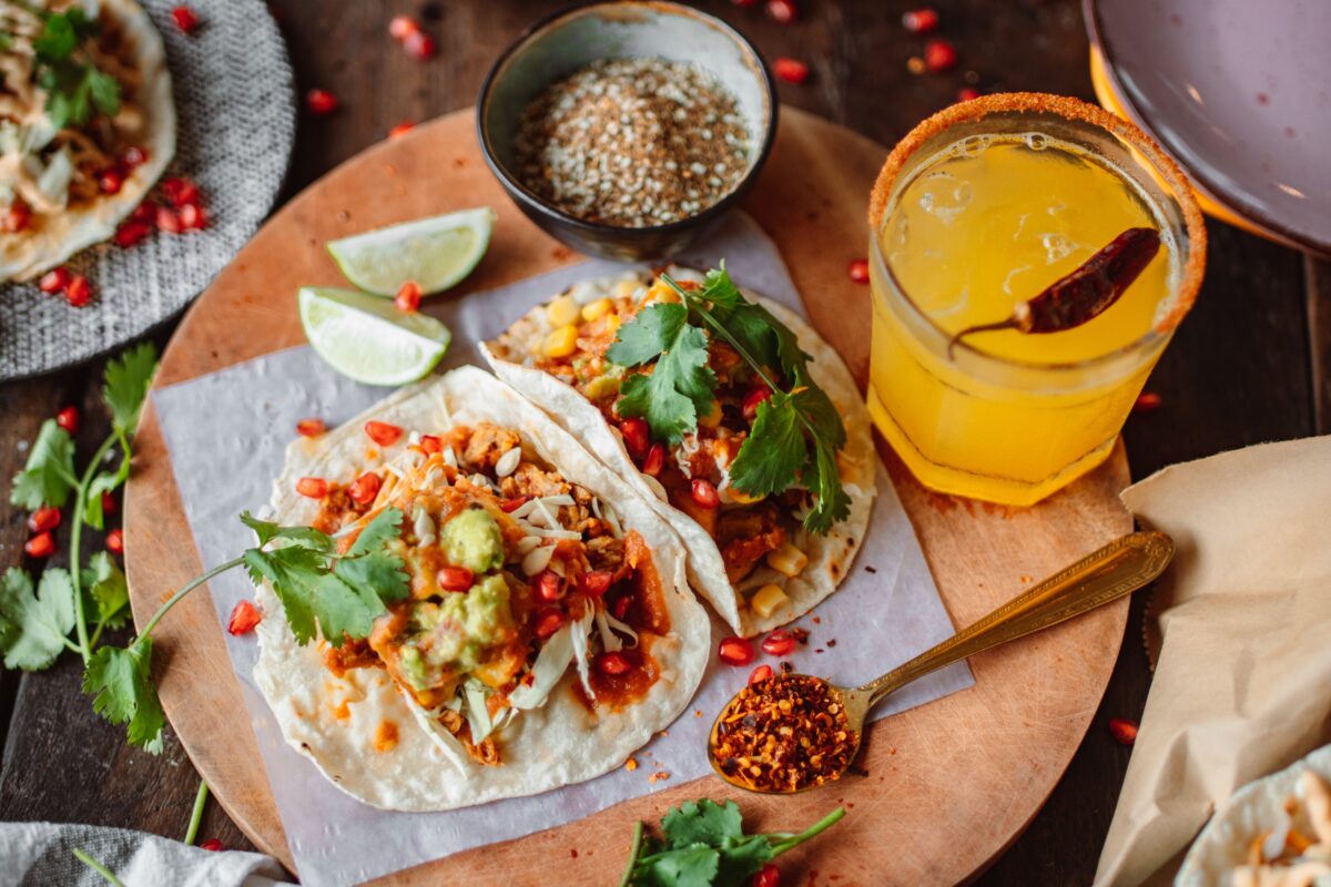 two fresh tacos on a cutting board with Mexican delicacies