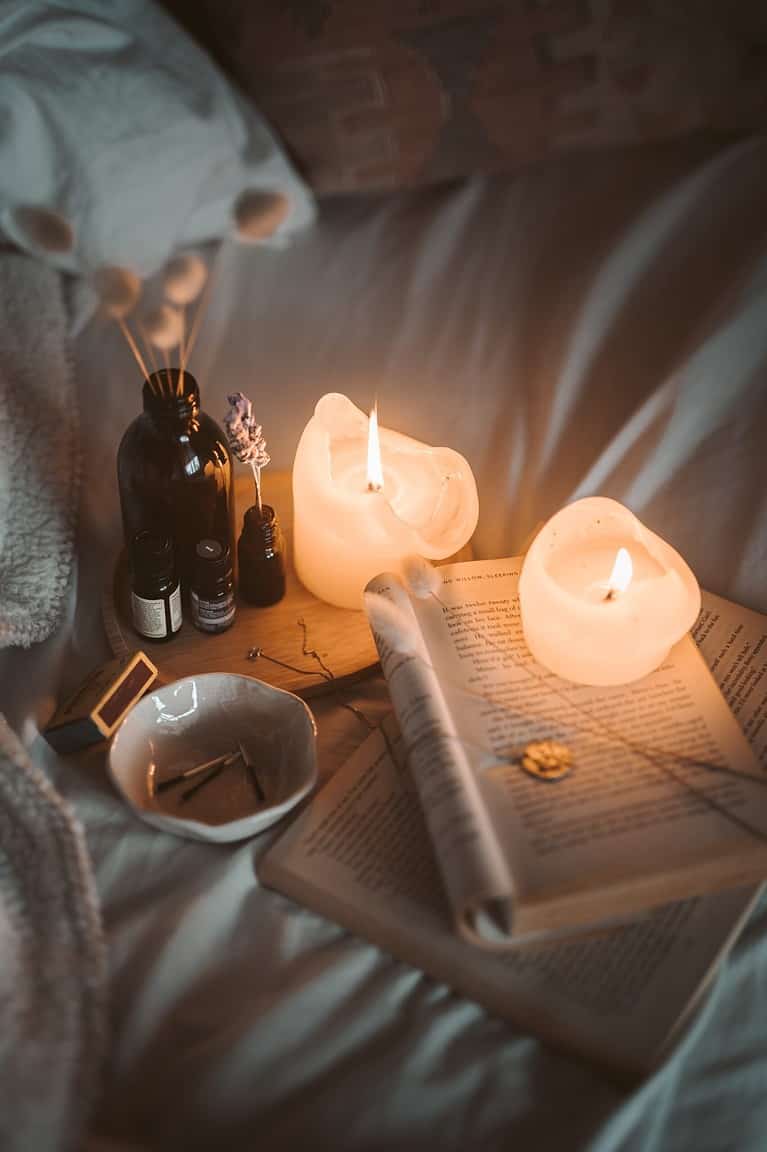a journal, essential oils, and candles on a soft white bedding