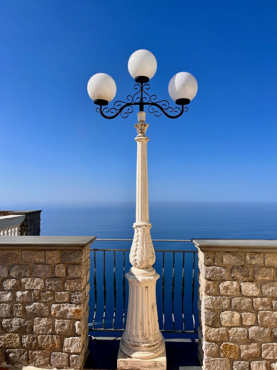 a vintage exterior lamp with three rounded bulb on a metallic foot with panoramic views on the Amalfi Coast in Italy