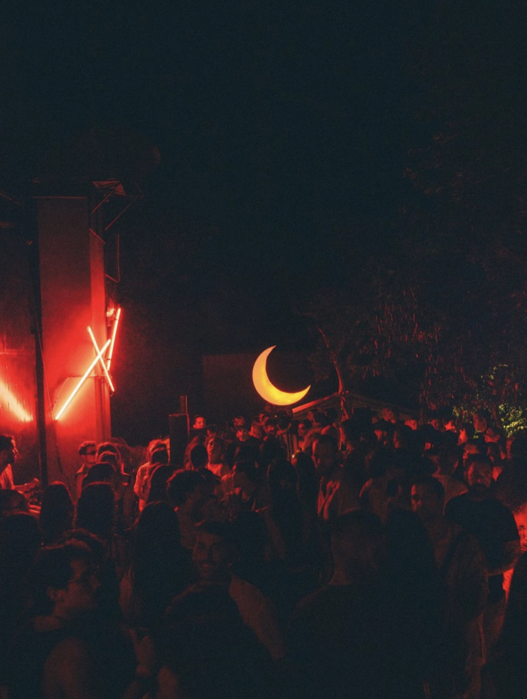 a crowd of people dancing in a open-air location in Tulum with neon signs