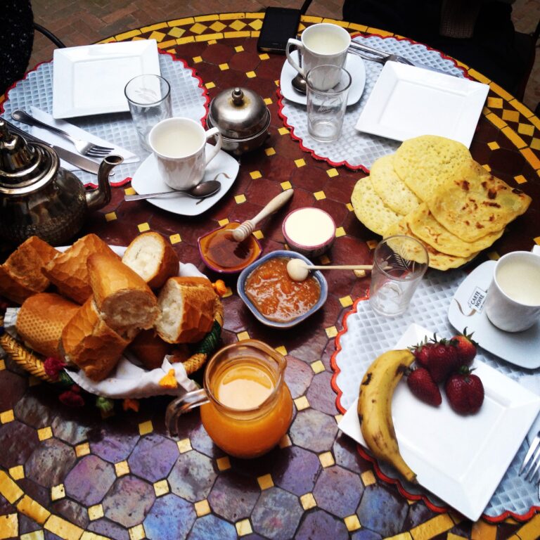 A traditional Moroccan breakfast including mint tea, msemen or baghrir pancakes, olives, fresh bread, honey, homemade jams, and argan oil.