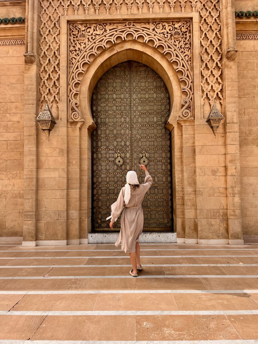 a woman in a long dress in front of an arabic majestic door
