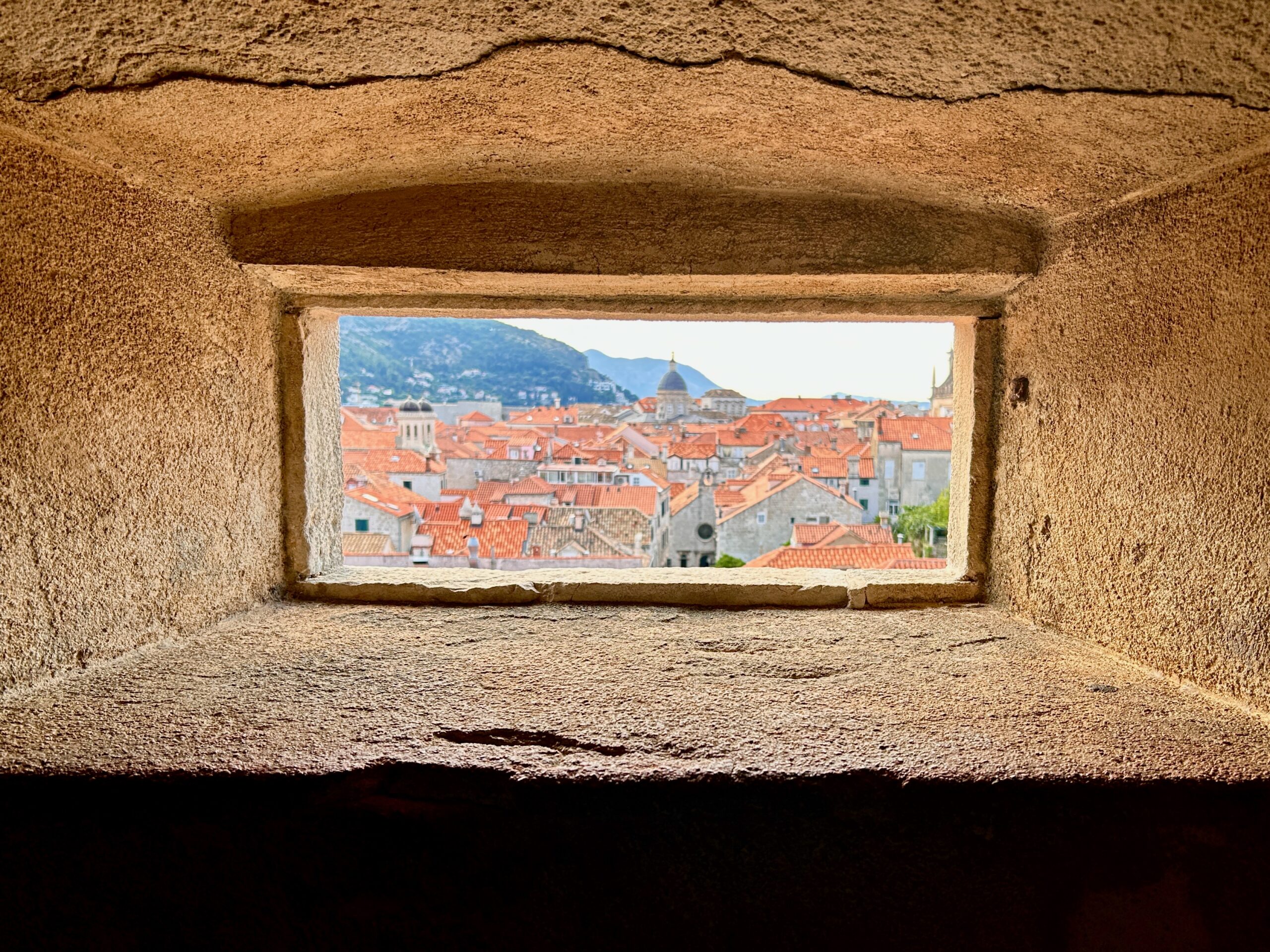 a view of the old town of Dubrovnik through a stone window of its city walls