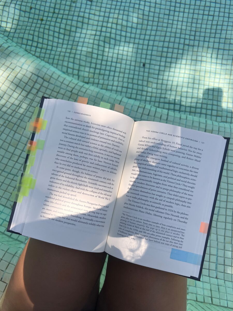 The book "Notes on Complexity" opened on the lap of a person standing by a pool.