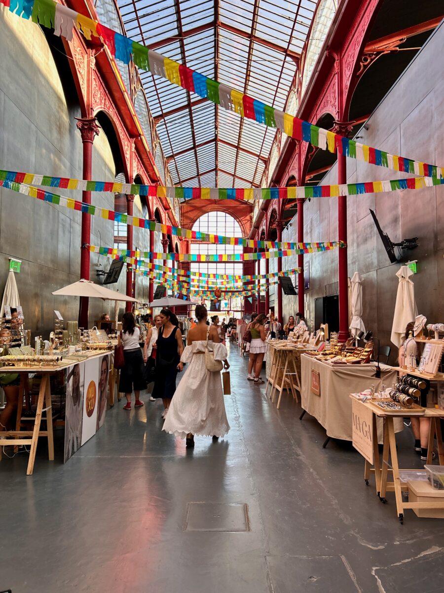 a woman wandering through an indoor shopping gallery with vendors and festive decoration, under a glass ceiling.