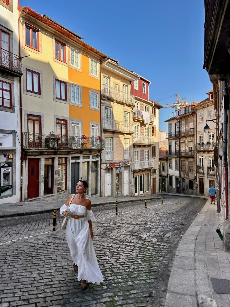 a woman in a long white dress walking up a picturesque street in Portugal