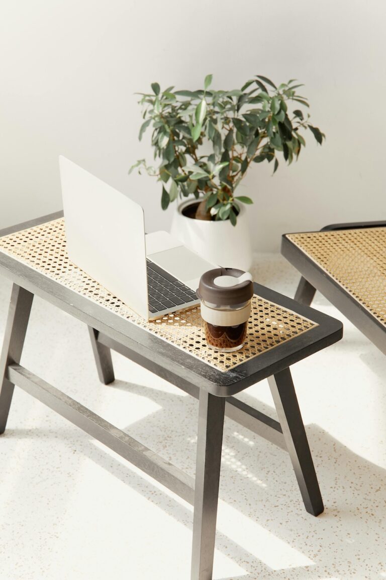 a small side table holding a laptop and a to-go mug