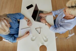 two women at a table using a laptop to brainstorm communications ideas