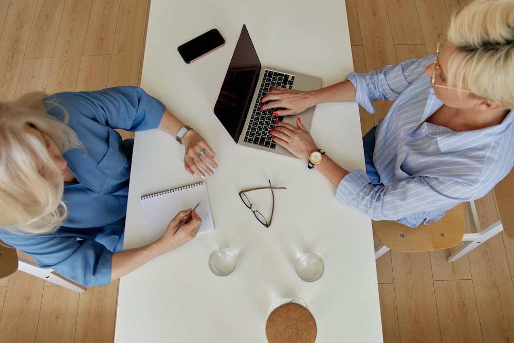 two women at a table using a laptop to brainstorm communications ideas