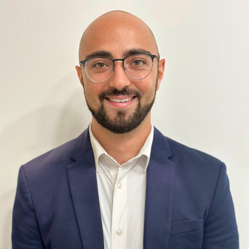 The portrait shot of a male solutions engineer wearing a suit and glasses.