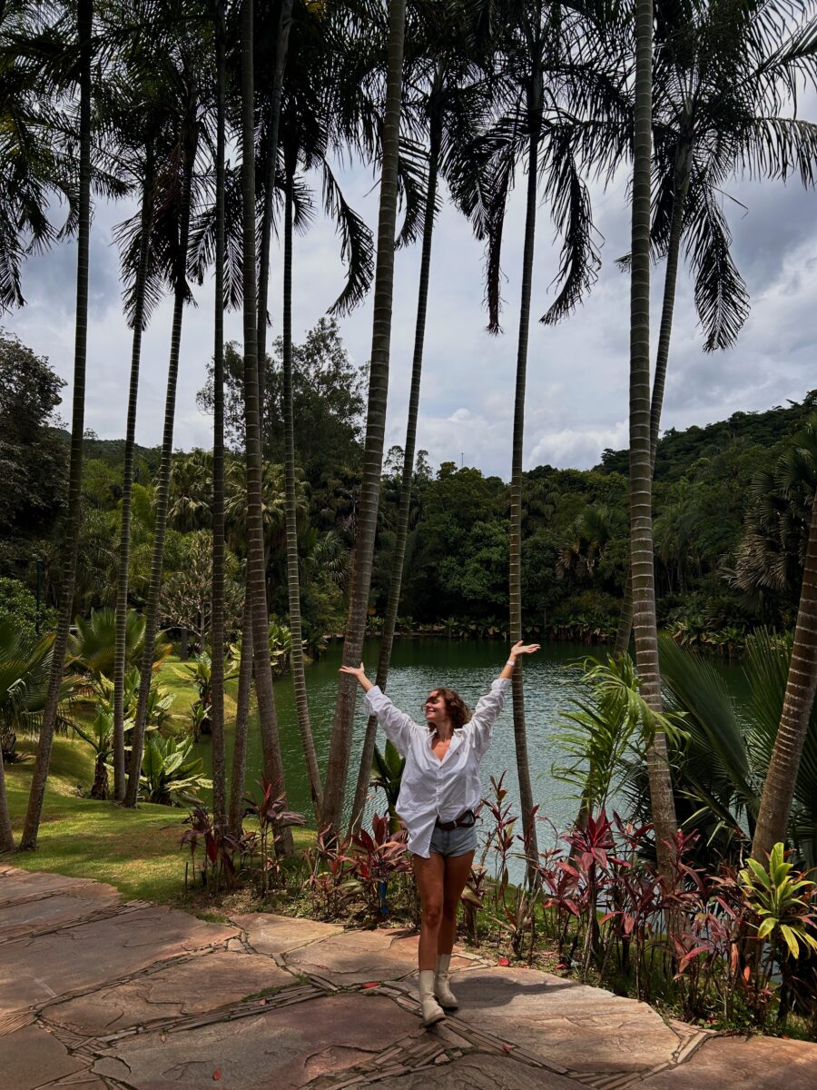 a woman standing in front of a lush garden with a lake at Inhotim in Minas Gerais
